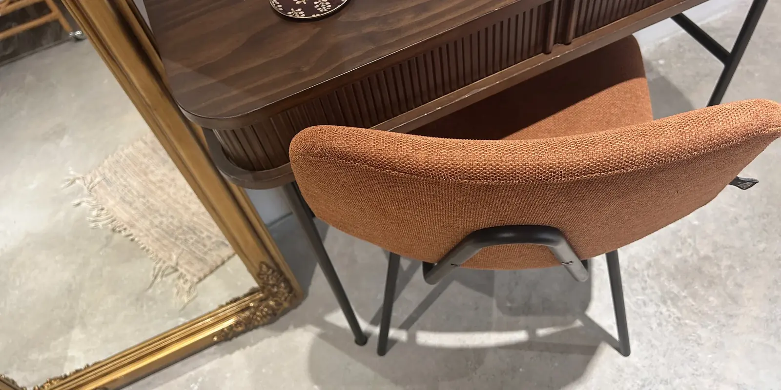 Bureau en bois cannelé, chaise en tissu terre cuite et miroir doré sur sol de béton